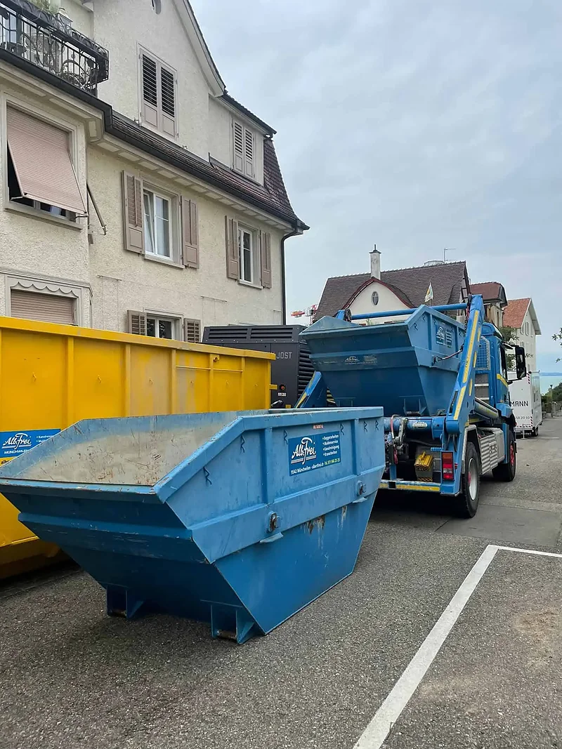 Welaki-Mulden vor einem Wohnhaus, daneben der Muldenwagen