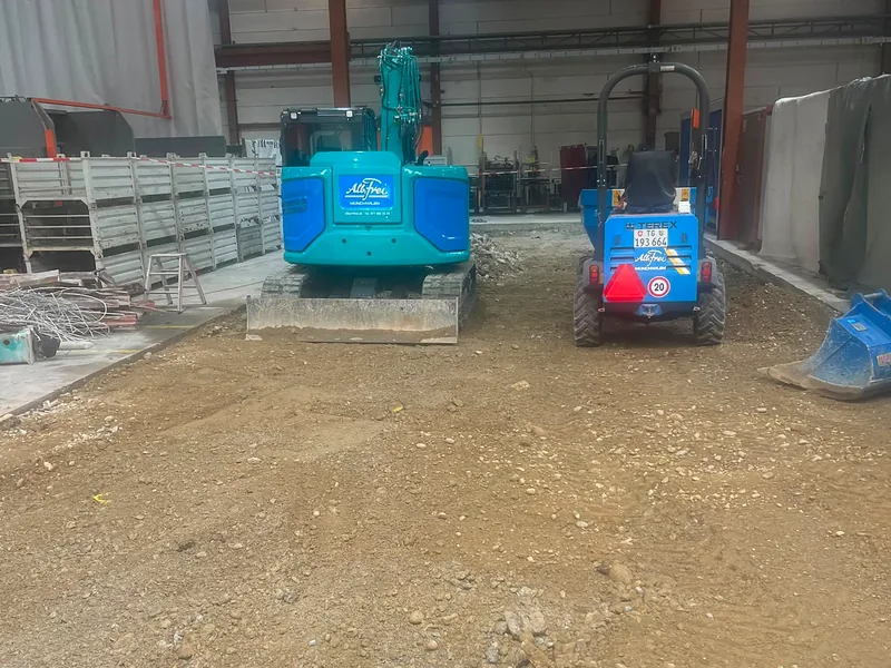 Kompaktbagger und Dumper beim Aushub in einer Halle